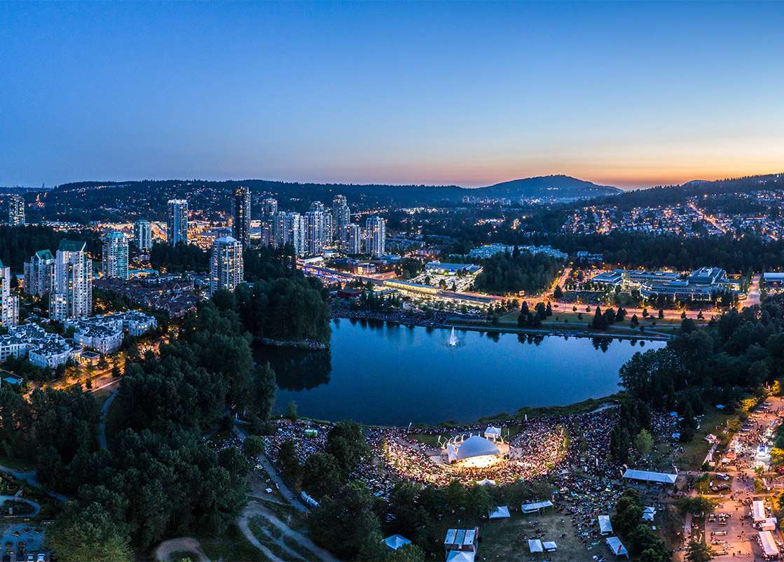 Coquitlam at dusk, with towers, a lake, and an outdoor stage